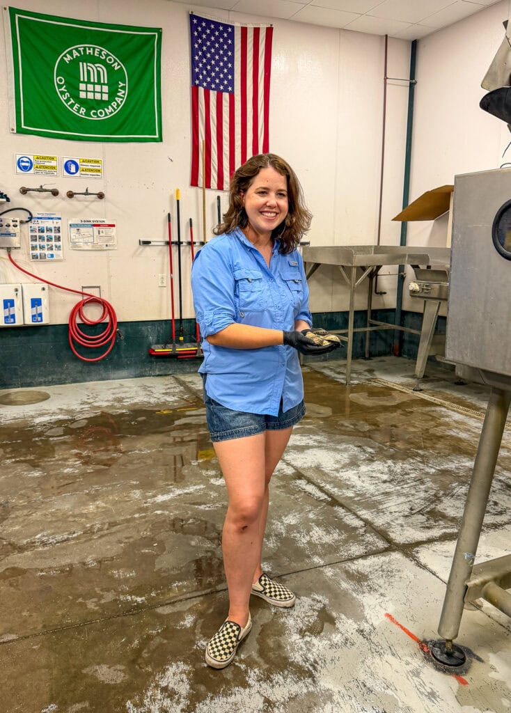 Smiling woman at Matheson Oyster Company with American flag and green banner behind her.